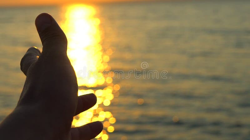 Man hand at sunset on sea, ocean beach. A man`s hand in sun`s rays on background sea water in nature. Glare of evening