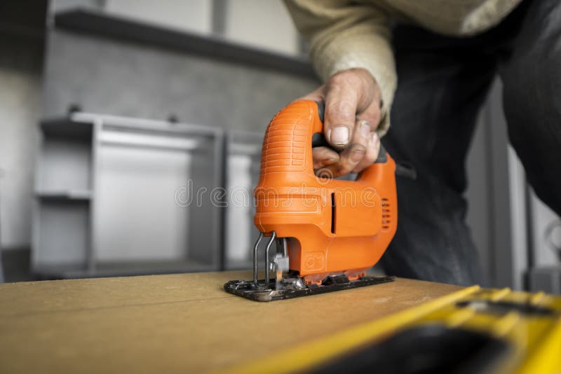 Man Hand Using Electric Jigsaw for Cutting a Fiberboard on a Back Side