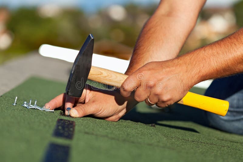 Man hands fastening bitumen roof shingles