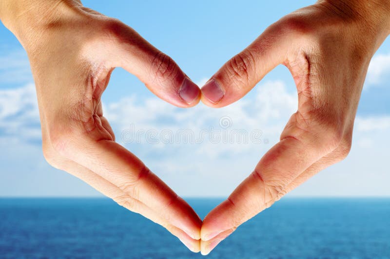 Man hands forming a heart with the ocean and the sky in the background