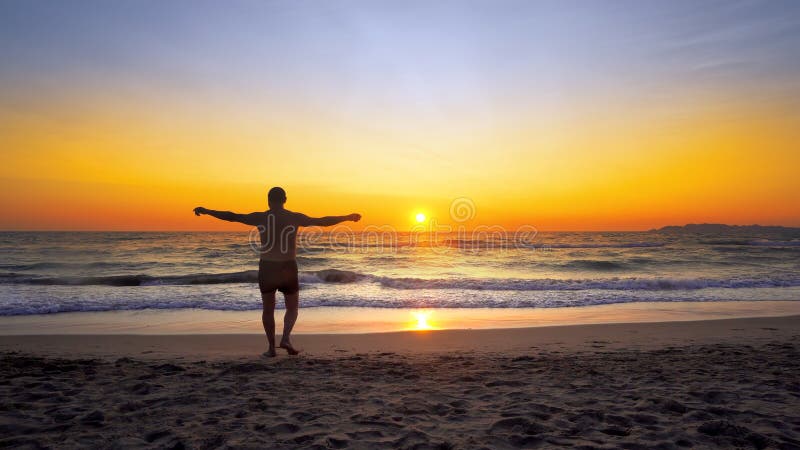 Man with hands wide open in VICTORY pose walks on empty ocean beach into water stock photos