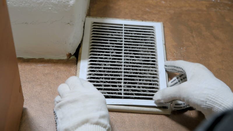 Man in handschoenen opent een stoffige ventilatie-grill
