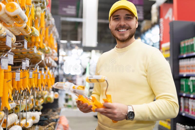 A Man in a Hardware Store Picks Up a Roller and Brushes for Painting