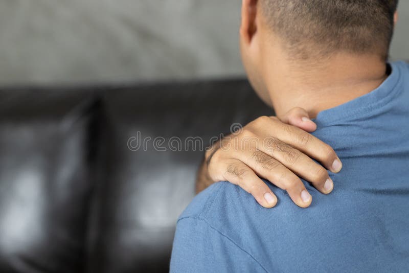 Man Has Neck Pain, Shoulder Pain Sitting on Sofa at Home Stock Photo