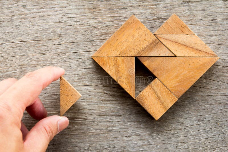 Man held piece of tangram puzzle to fulfill the heart shape on wooden table Concept of love