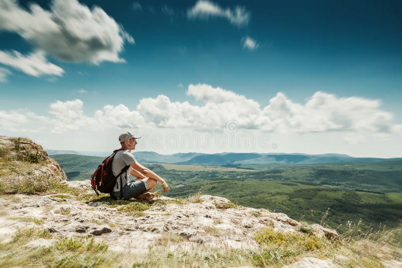 Man hiker with backpack relaxing on top of a mountain