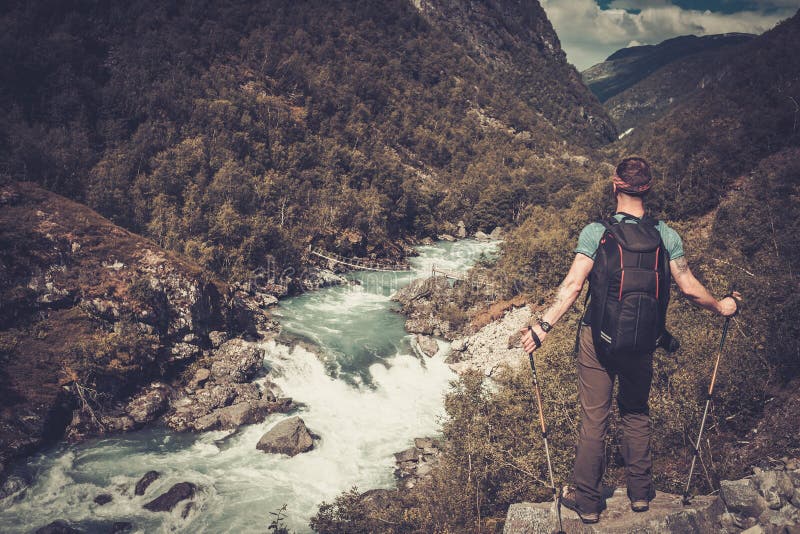 Man hiker with backpack standing on the edge of the cliff with epic wild mountain river view.