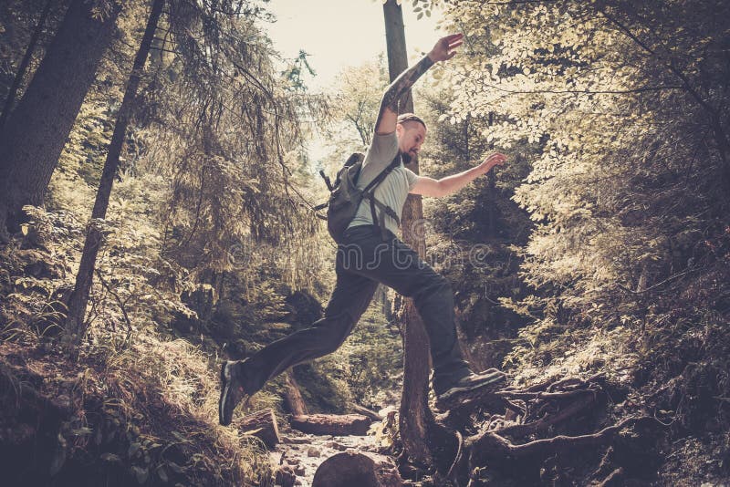 Man hiker jumping across stream