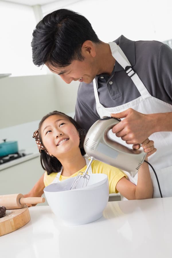 Man with His Daughter Using Electric Whisk into Bowl in Kitchen Stock