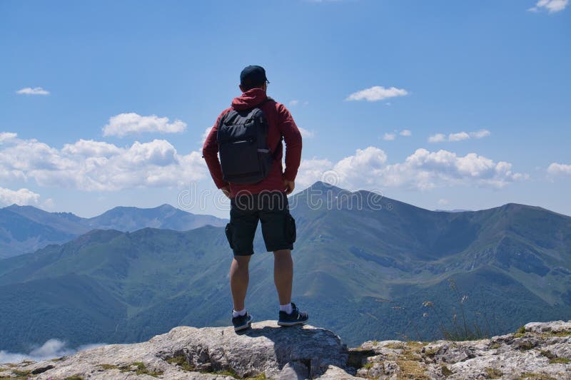 Man in his 30s with a backpack stands on a mountain peak, overlooking a vast landscape royalty free stock photography