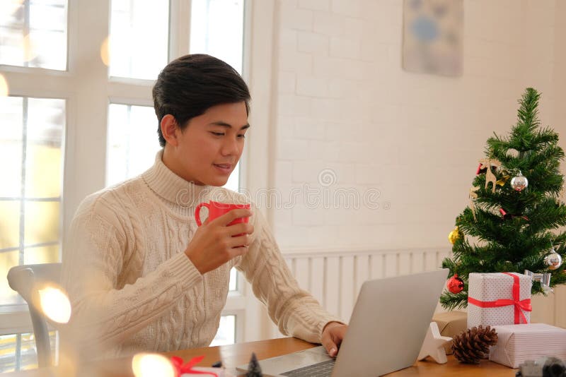 Man holding coffee cup & using computer at home during christmas stock images