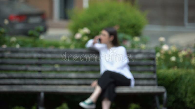 Man holding female photo, watching at girl talking phone on bench, stalker