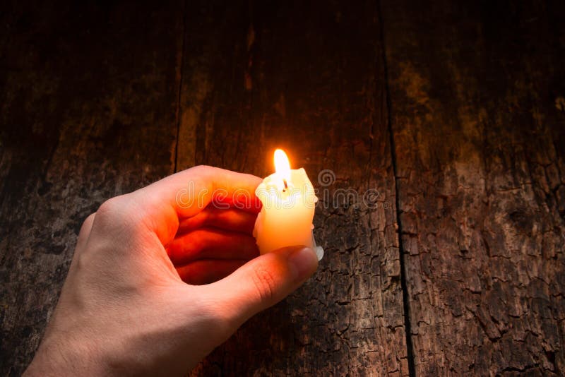 Man holding in his hand a lighted wax candle on a wooden