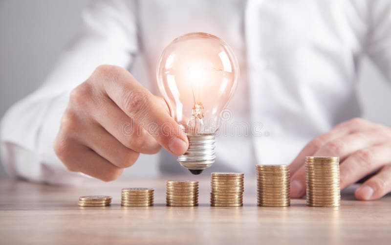 Man holding light bulb. Stack of coins on the desk. Saving energy and money stock photo