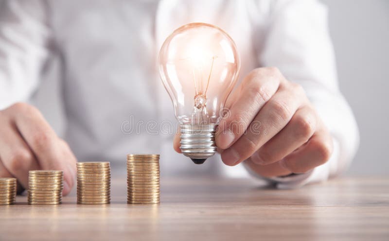 Man holding light bulb. Stack of coins on the desk. Saving energy and money royalty free stock photo