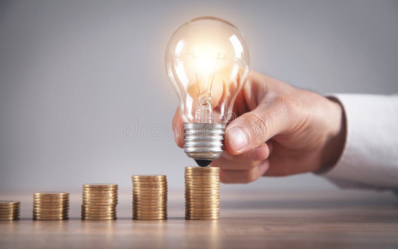 Man holding light bulb. Stack of coins on the desk. Saving energy and money stock photo