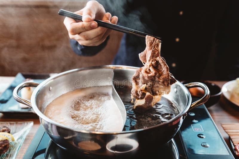 Man holding medium rare slice Wagyu A5 beef out from hot pot shabu shoyu soup base by chopsticks with steam