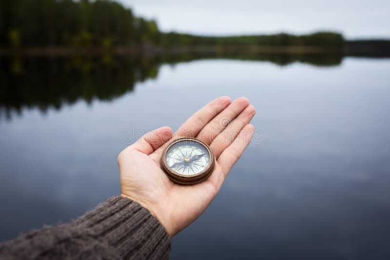 Man holding an old compass in hand. Lake and island on background.