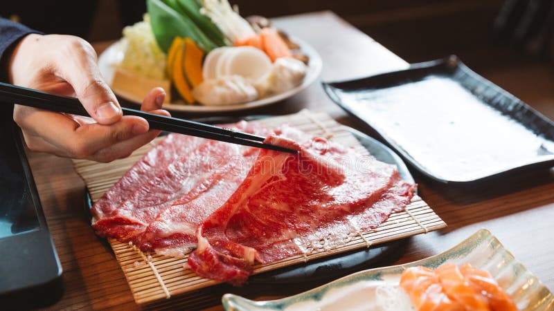 Man holding rare slice Wagyu A5 beef by chopsticks for boiling in Shabu hot pot