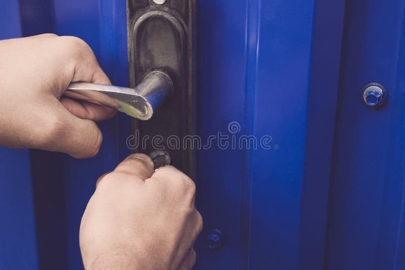 The man holds the door handle and opens the gate with a key.