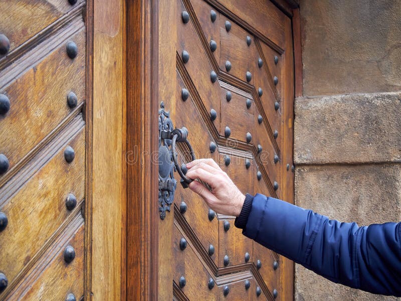 Man holds door knocker from old wooden door in hand. He knocks on the locked door