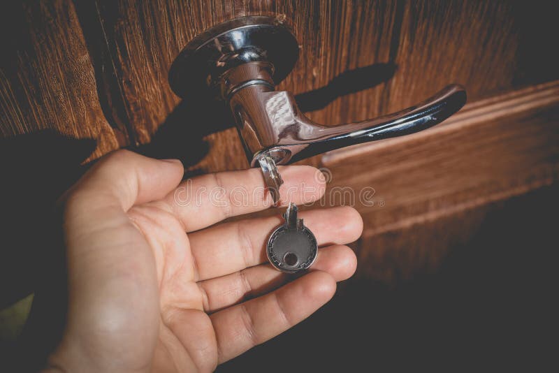 A man holds in his hand a small light broken key against the background of a door lock