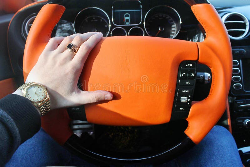 A man holds the steering wheel of a luxury car. Gold watch and a ring on his hand