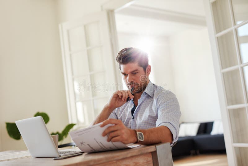 Man at Home Office with Laptop and Reading Documents Stock Photo