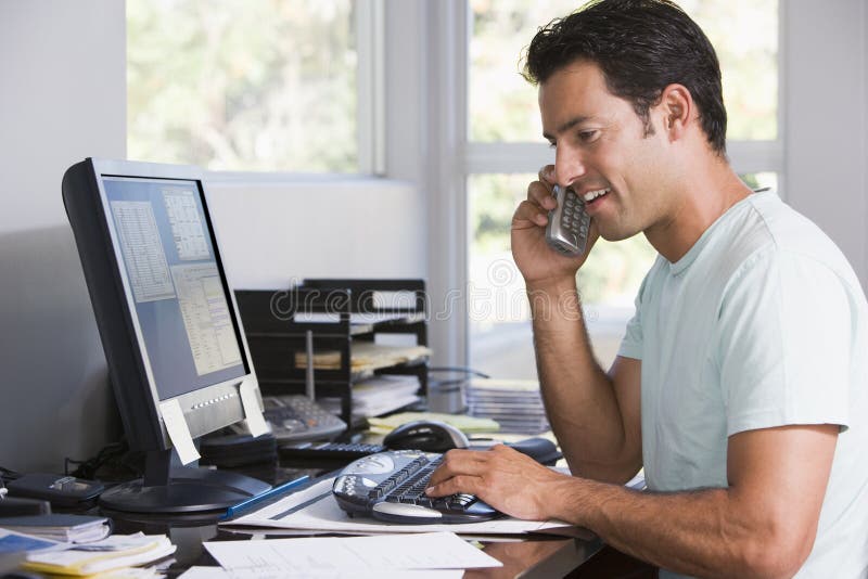 Man in home office on telephone using computer and smiling