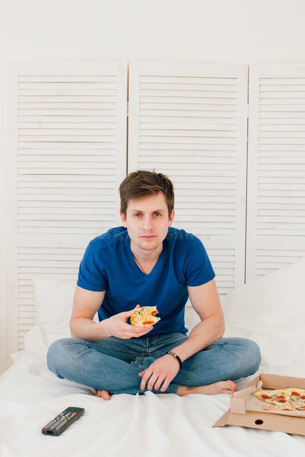 Man hållande ögonen på TVsammanträde på sängen och ätapizza royaltyfria bilder Man hållande ögonen på TVsammanträde på sängen och ätapizza royaltyfria bilder