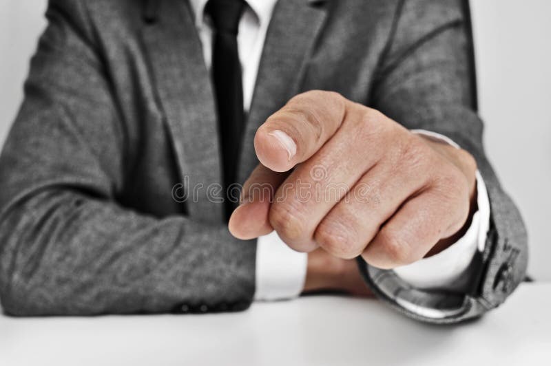 Man wearing a suit sitting in a table pointing the finger to the observer. Man wearing a suit sitting in a table pointing the finger to the observer