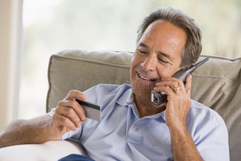 Man indoors using telephone looking at credit card stock photography