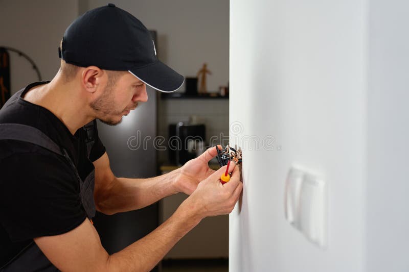 Man installing electrical wall switch and connecting wires inside white wall using screwdriver. Concept of electrician work, home renovation, electrical installation and maintenance. Home electrician stock images, royalty-free photos and pictures
