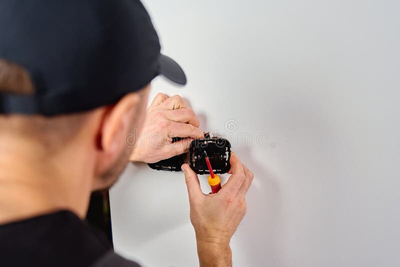 Man installing electrical wall switch and connecting wires inside white wall using screwdriver. Concept of electrician work, home renovation, electrical installation and maintenance. Home electrician stock images, royalty-free photos and pictures
