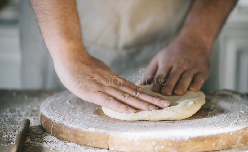 Man kneading and baking homemade pizza dough in the kitchen. Closeup on baker`s hands preparing loaf of bread