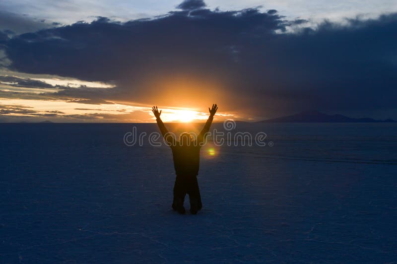 Muž kľačiaci ramená otvoriť a vyvýšený na púšť v bolívia na západ slnka.