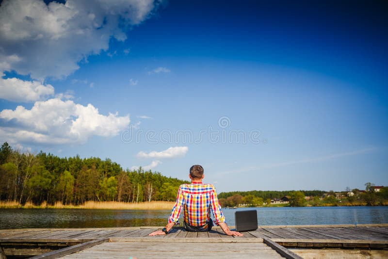 Man with laptop working outdoor near the beautiful lake