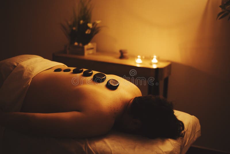 Man lies in a spa with black stones on his back