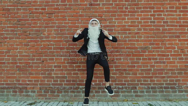 Man like a Santa Claus is dancing, Merry christmas and New year 2019, red brick wall as background