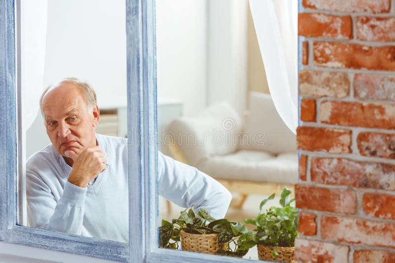 Senior man looking out of window in a loft flat stock photo