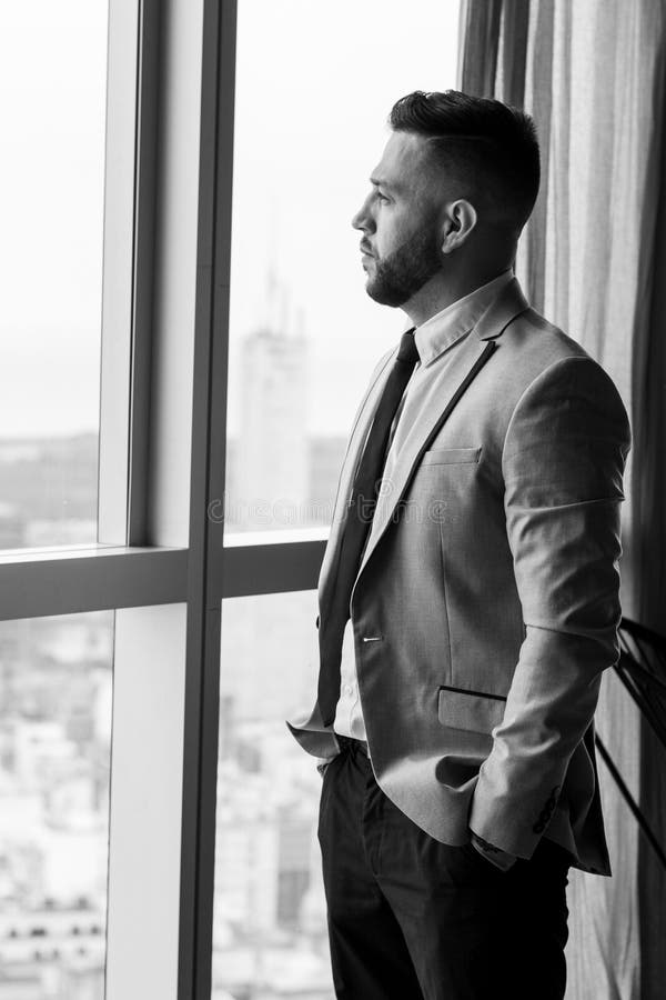 man looking through the window of a tall building wearing a suit