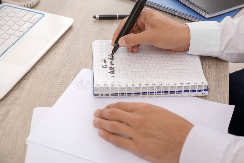 Man making to-do list while sitting at table, closeup stock photo Man making to-do list while sitting at table, closeup stock photo