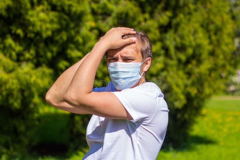 A man in a mask from allergy, in a white T-shirt, stands in the park stock images A man in a mask from allergy, in a white T-shirt, stands in the park stock images