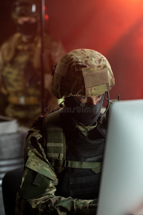 Man in mask, helmet and camouflage uniform looking at computer monitor royalty free stock image