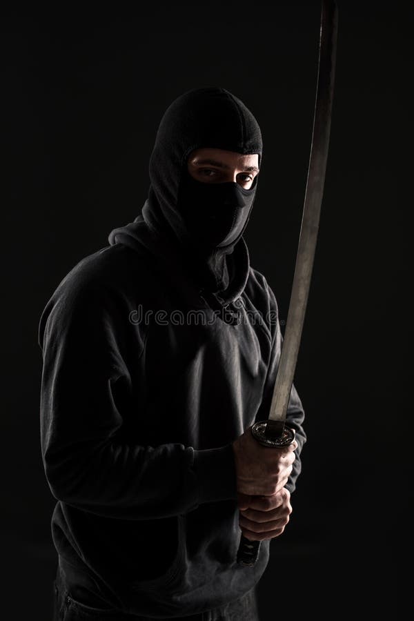 Man med balaclavaen och katanasvärdet på svart bakgrund arkivfoton Man med balaclavaen och katanasvärdet på svart bakgrund arkivfoton