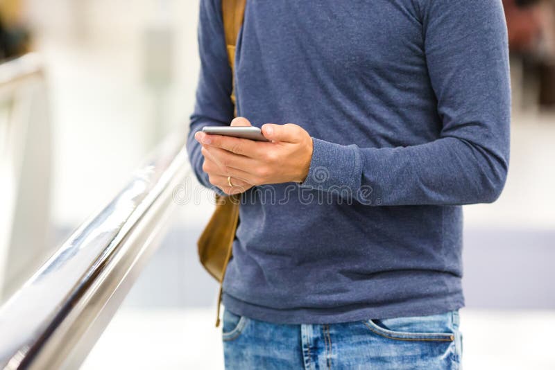 Man med den hållande mobiltelefonen för ryggsäck på flygplatsen royaltyfri bild Man med den hållande mobiltelefonen för ryggsäck på flygplatsen royaltyfri bild