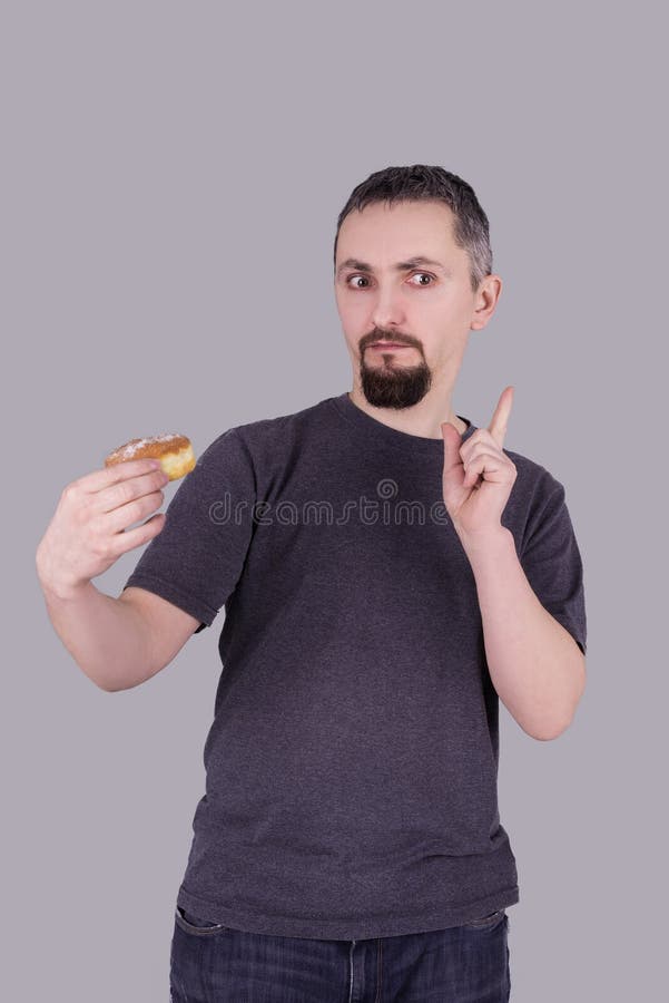 Man med ett skägg som äter en bulle över grå bakgrund arkivfoto Man med ett skägg som äter en bulle över grå bakgrund arkivfoto