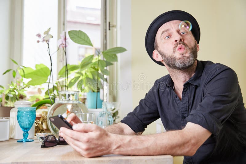 Man med hatten och telefonen och såpbubblor för skägg den lyckliga seende I arkivbilder Man med hatten och telefonen och såpbubblor för skägg den lyckliga seende I arkivbilder