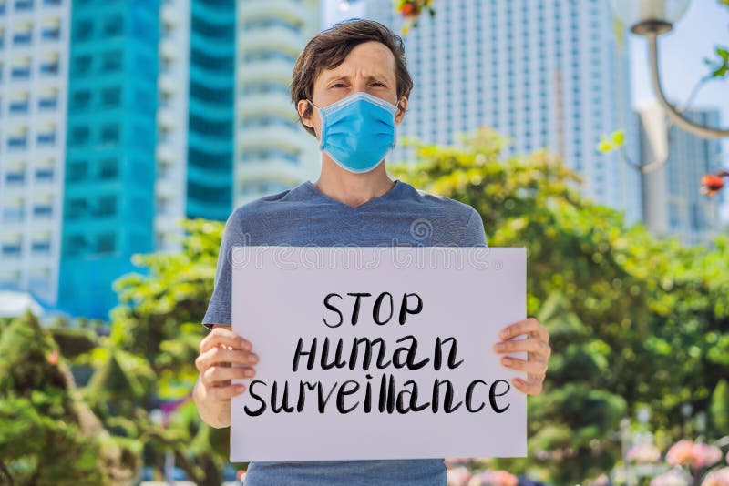 Man in medical mask prevents coronavirus disease holds a poster stop human surveillance Hand written text - lettering