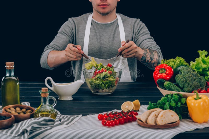 man with tattoo mixing ingredients in bowl on table with vegetables